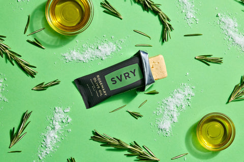 SVRY rosemary olive oil protein bar with rosemary sprigs, olive oil and sea salt on a green background