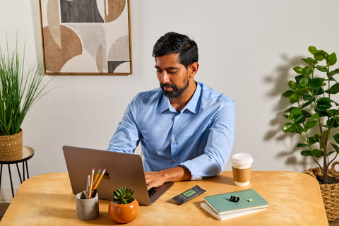 Man working on a laptop at a desk with a rosemary olive oil SVRY protein bar next to him