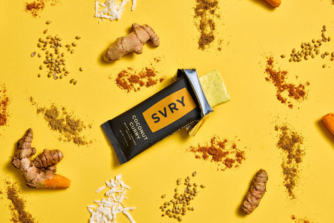 SVRY supplement bar surrounded by turmeric roots and seeds on a yellow background