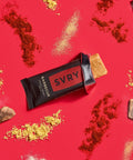 SVRY barbecue protein bar surrounded by spices, garlic cloves and smoked wood chips on a red background