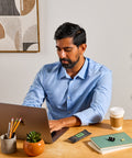 Man working on a laptop at a desk with a rosemary olive oil SVRY protein bar next to him