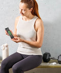 Woman holding a rosemary olive oil protein bar next to dumbbells on a bench at the gym