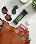 Brown leather handbag with sunglasses, keys, SVRY bar, and white earbuds on a light surface.