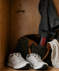 a SVRY taco protein bar is sticking out of a gym bag in a locker that also has a gym towel, sneakers, a water bottle and a sweatshirt hanging on a hook in the back
