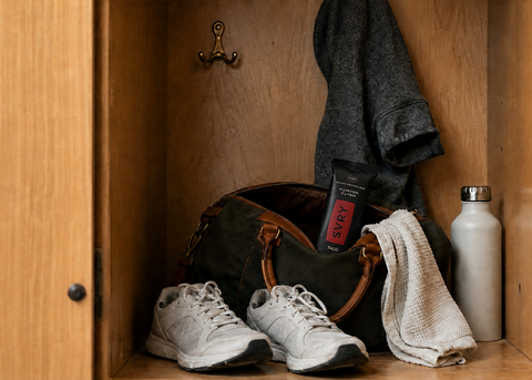 a SVRY taco protein bar is sticking out of a gym bag in a locker that also has a gym towel, sneakers, a water bottle and a sweatshirt hanging on a hook in the back