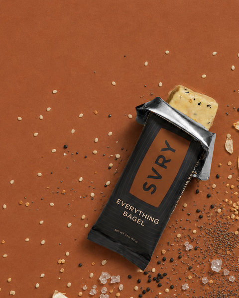 SVRY Everything Bagel protein bar on a brown background with garlic pieces and spices.