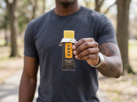 Person holding a SVRY coconut curry protein bar outdoors