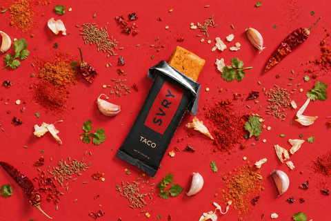 SYVR Taco protein bar surrounded by spices and herbs on a red background